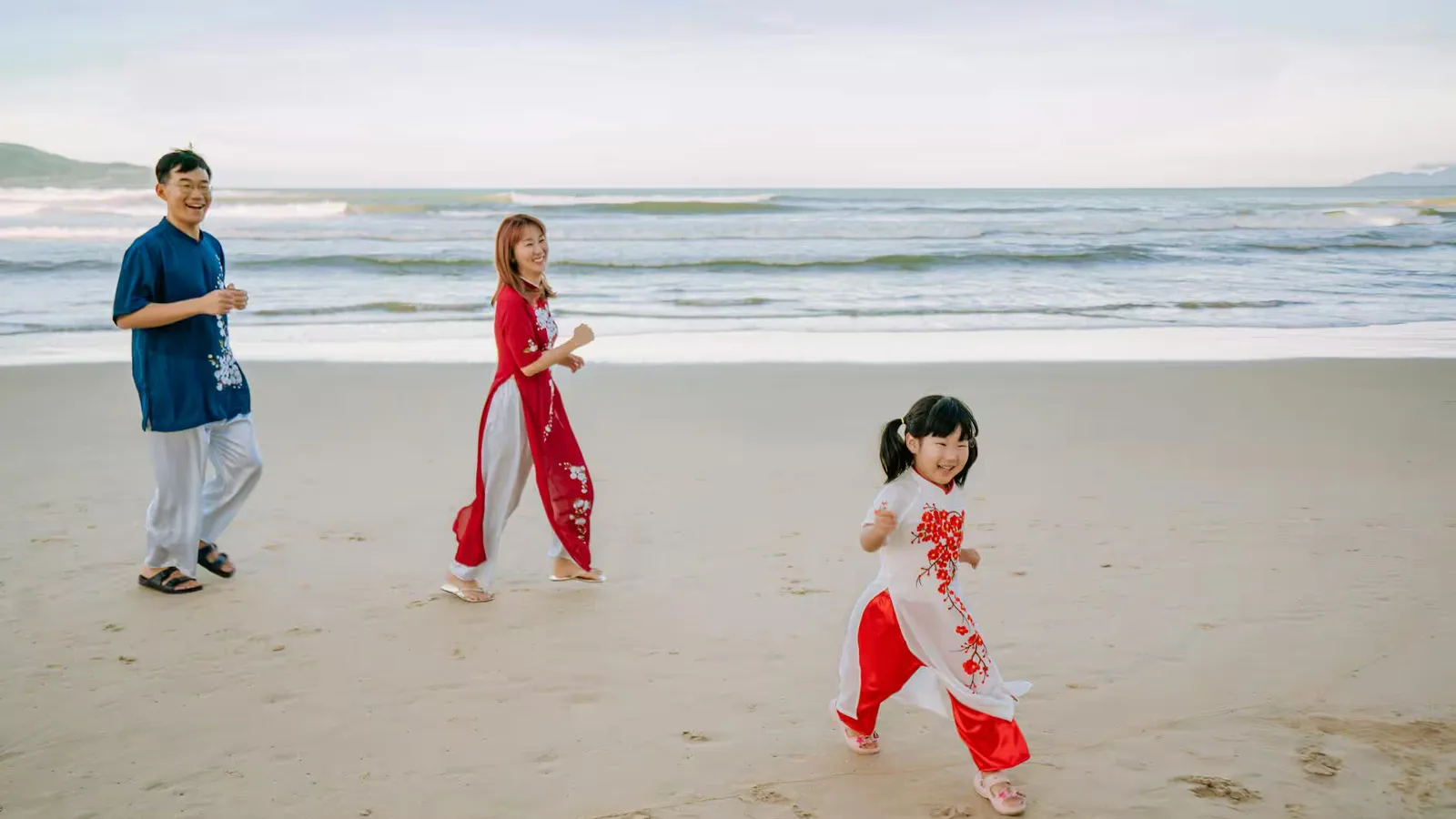 Asian family laughing and playing on a sandy beach during the day.