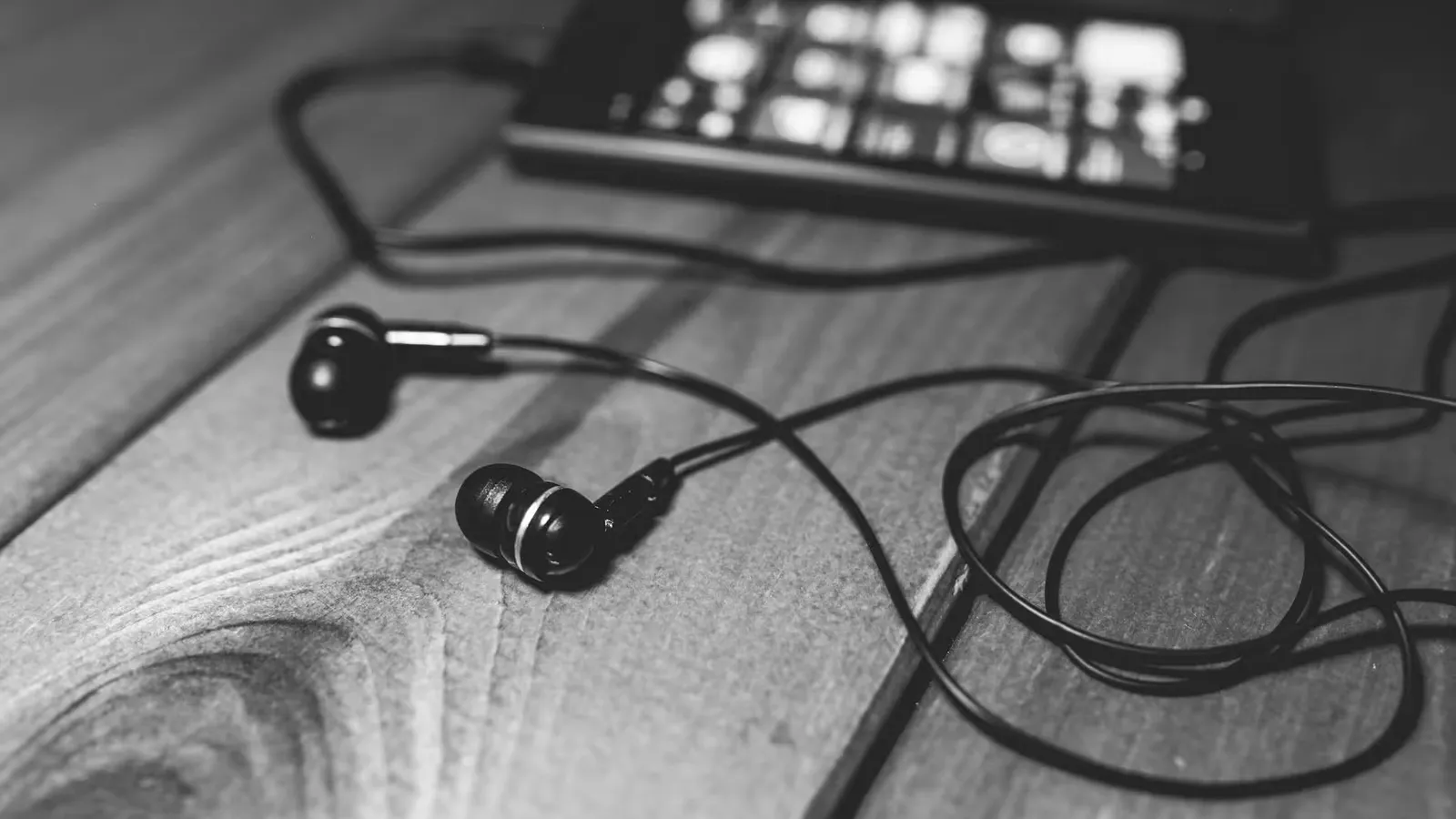 Monochrome image of earphones and smartphone on wooden table, showcasing a modern lifestyle.