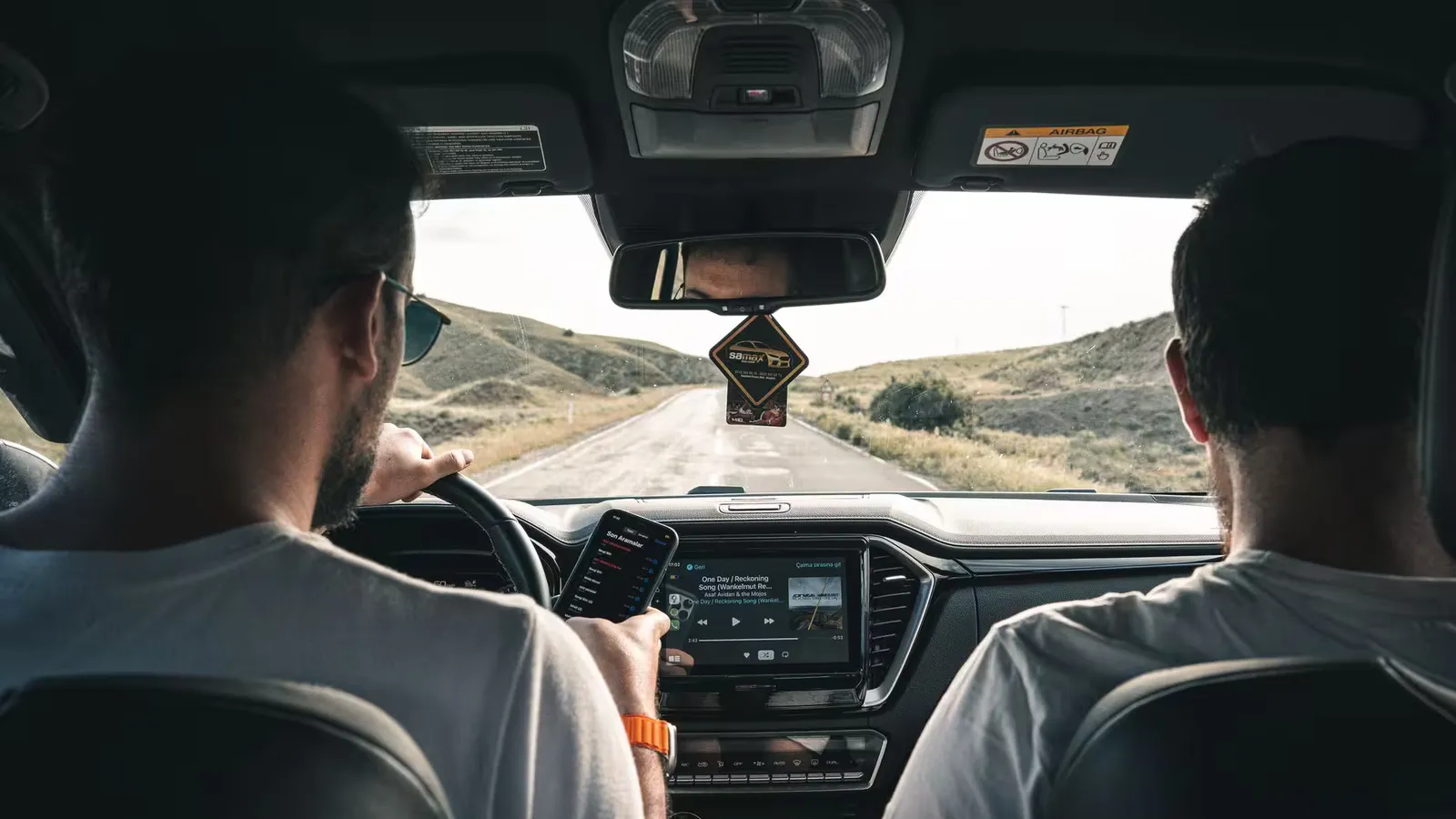Two men driving through a scenic landscape, using a cellphone for navigation.