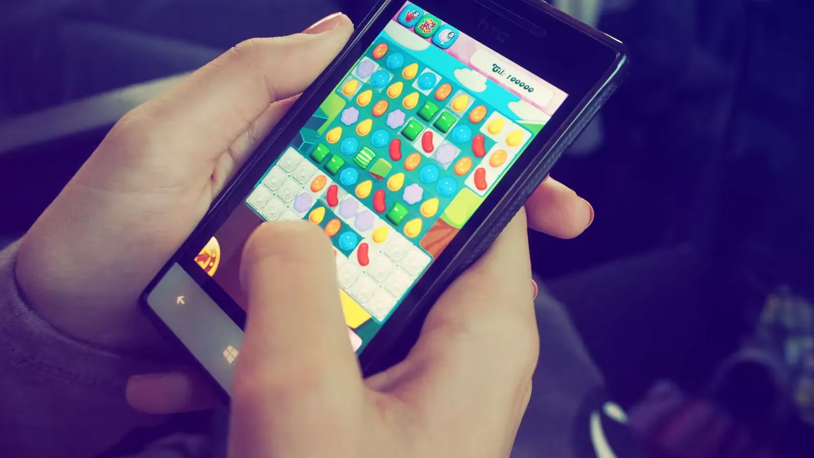 Hands holding a smartphone with a colorful puzzle game on the screen, displaying modern technology.