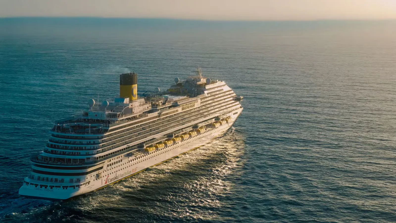 A breathtaking view of a cruise ship sailing across the ocean with the sun setting in the background.