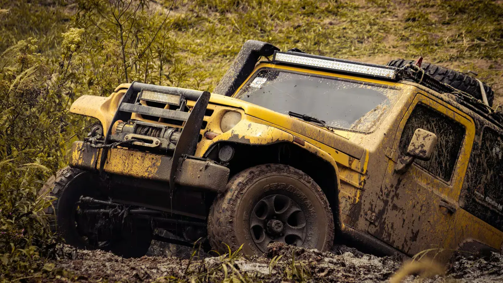 Yellow 4x4 SUV tackling a muddy off-road path in a rugged outdoor setting.