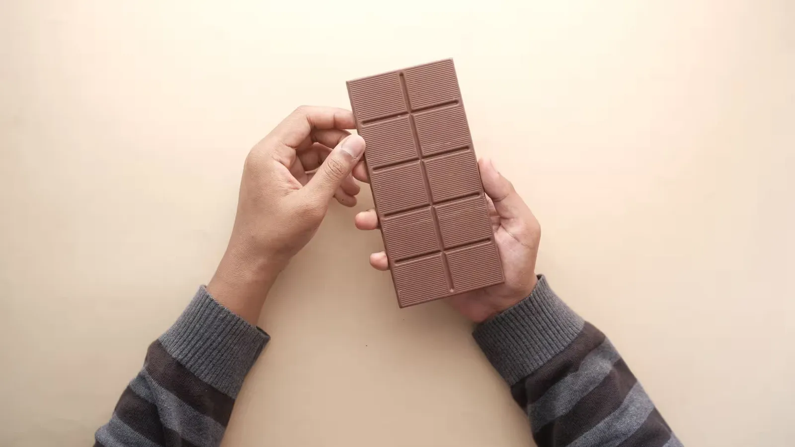 Close-up of hands holding a chocolate bar with a striped sweater, captured in natural light.