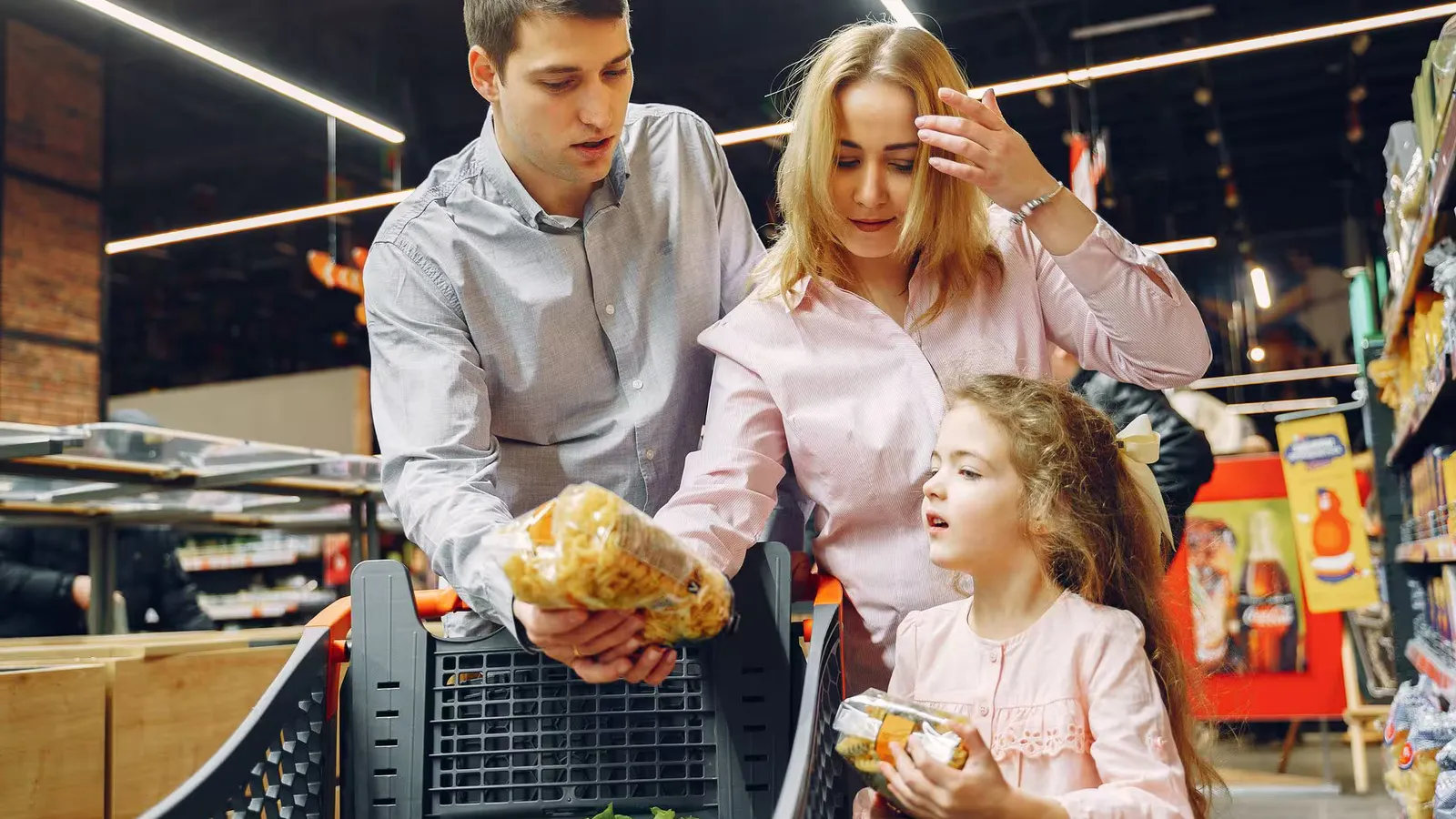 A family enjoying shopping in a supermarket aisle, selecting groceries with a cart.