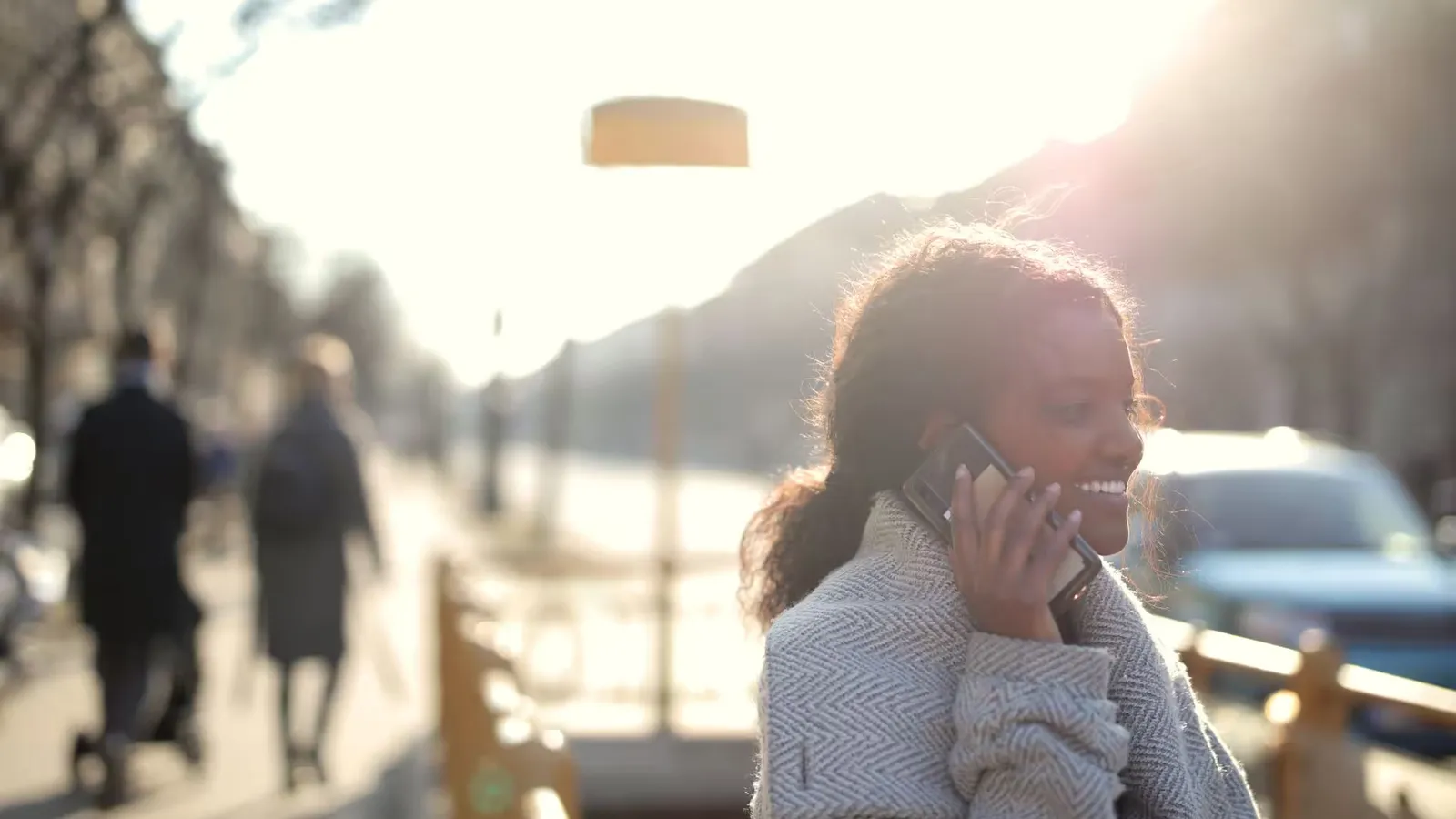 Smiling woman having a phone conversation outdoors with a bright sunny backdrop.