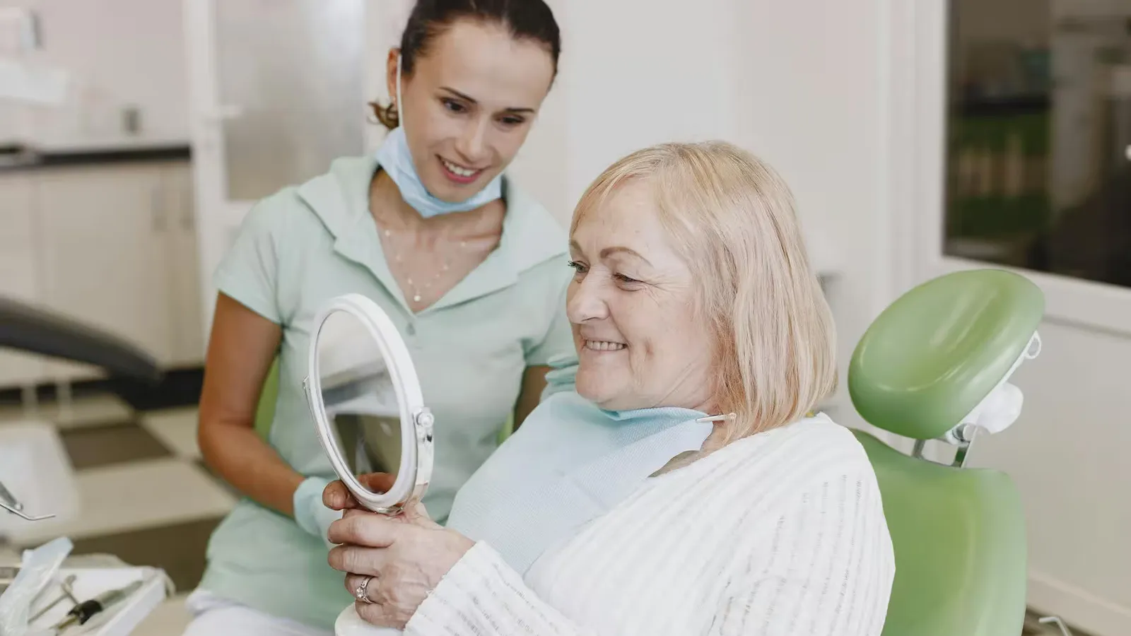Senior woman smiles while checking her teeth in a mirror with a dentist. Healthcare and dentistry concept.