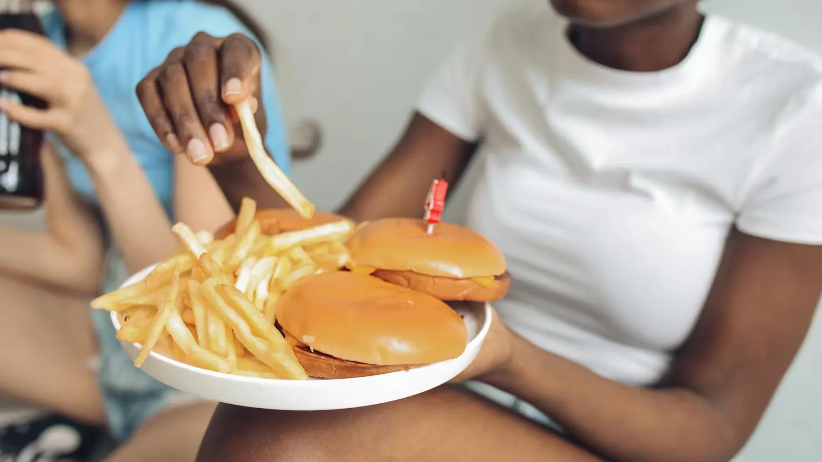 Two friends enjoying burgers and fries indoors, showcasing casual dining and happiness.