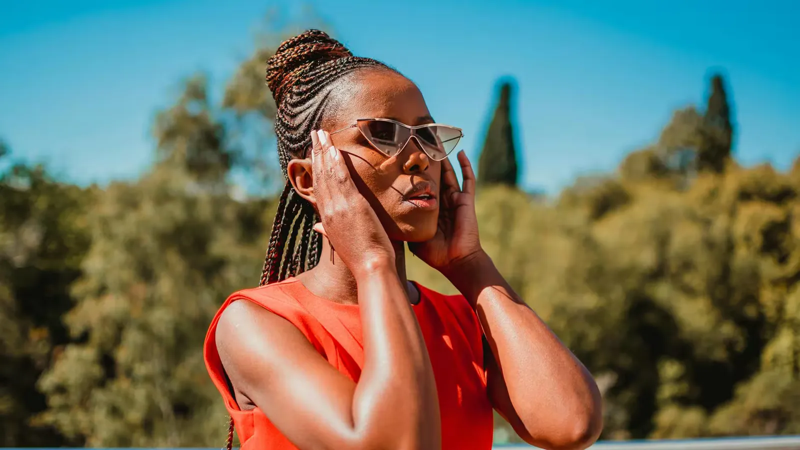 A fashionable woman in sunglasses enjoying a sunny day outdoors with a peaceful background.