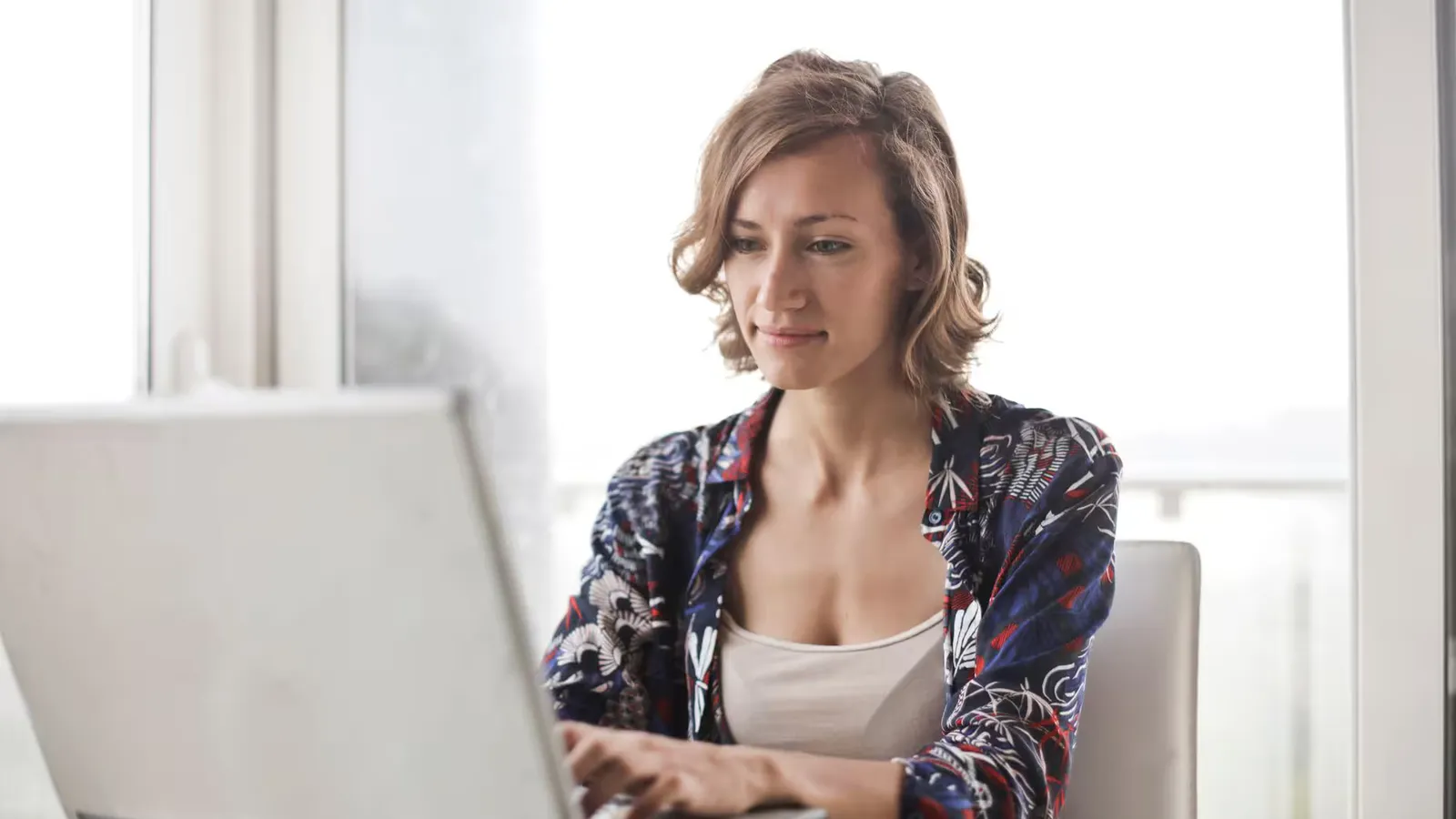 A woman typing on a laptop in a bright, modern home office setting.