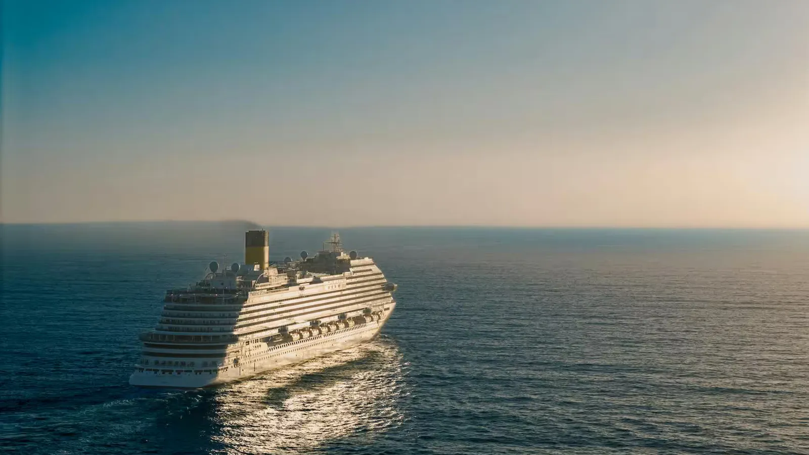 A cruise ship gracefully sails across the ocean at sunset, creating a tranquil scene.